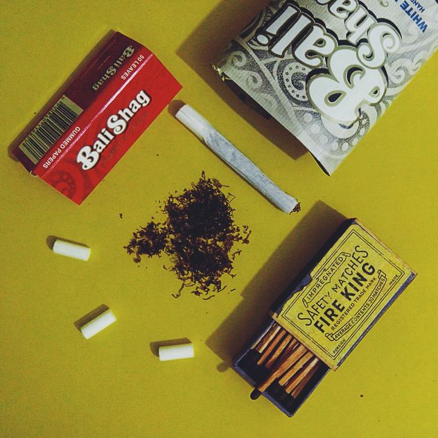 Rolled cigarette, tobacco, filter, cigarette paper and old matches over yellow background - Free image #272205