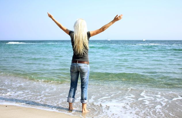 Young blond woman standing aback on sea shore - image #344075 gratis
