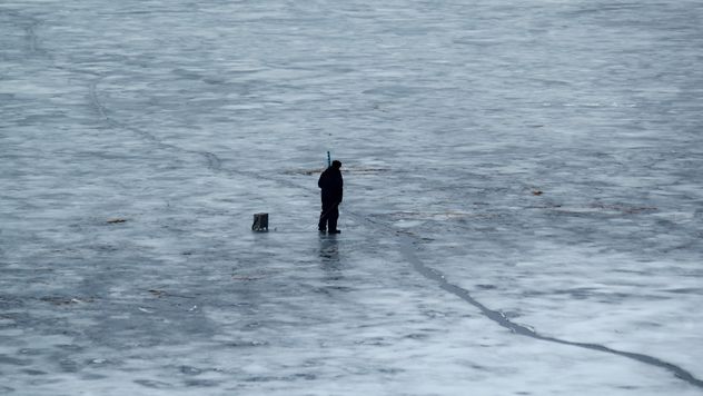 Fisherman during winter fishing on frozen river - бесплатный image #344625